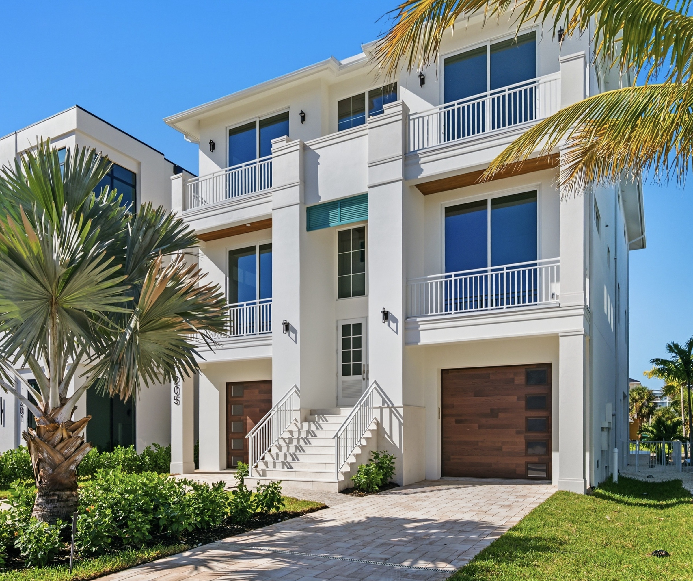 Three-story contemporary coastal custom home in crisp white stucco with warm wood-slat doors and mature palms — Coastal Residence by Afonova Nelson Homes