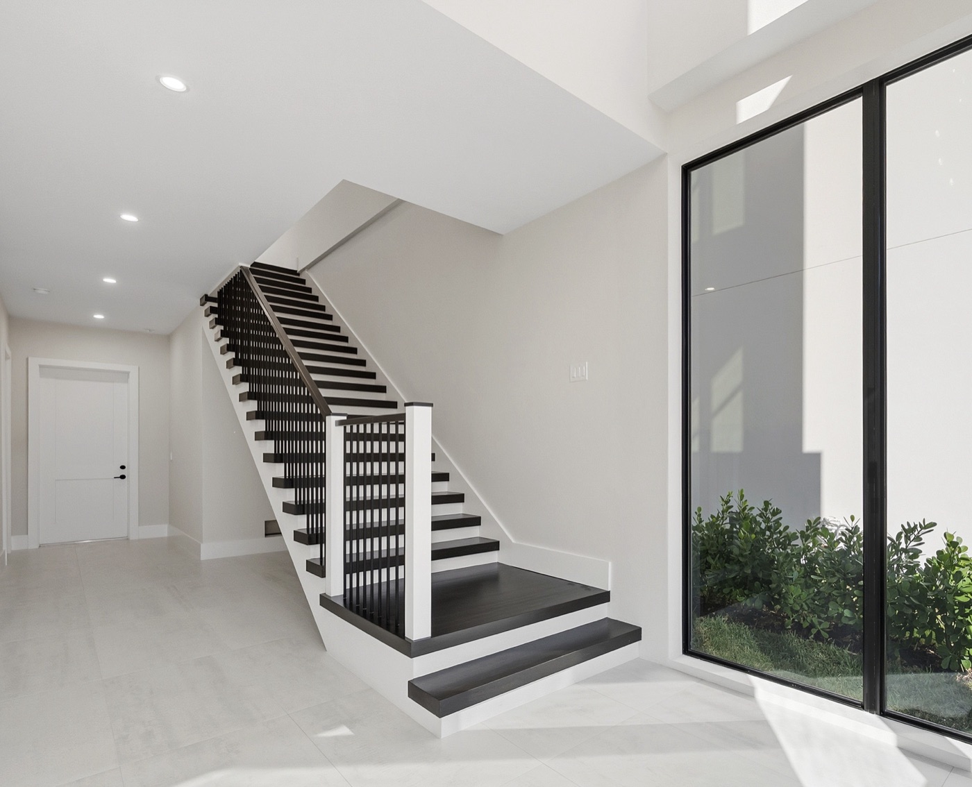 Sculptural floating staircase with ebony treads and black slatted railing against a two-story window wall — Modern Residence