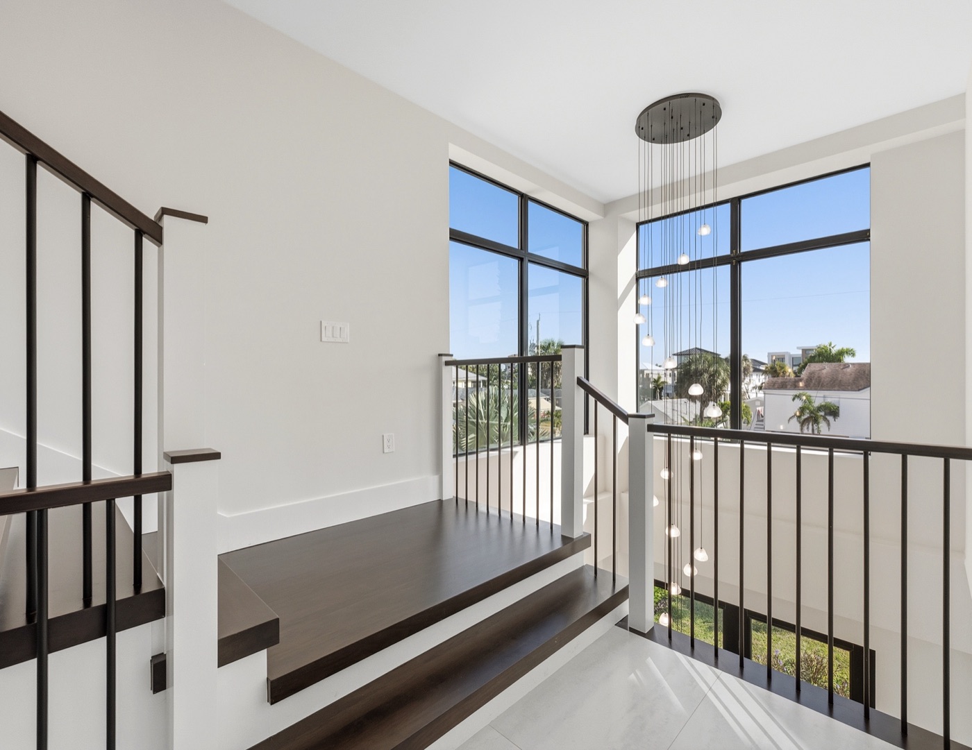 Staircase landing with dark wood treads and a sculptural cascading multi-pendant chandelier — Modern Residence